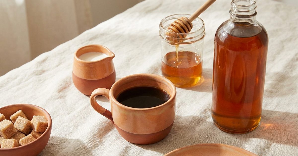 Black coffee with cream, sugar cubes, honey and an unlabeled syrup bottle