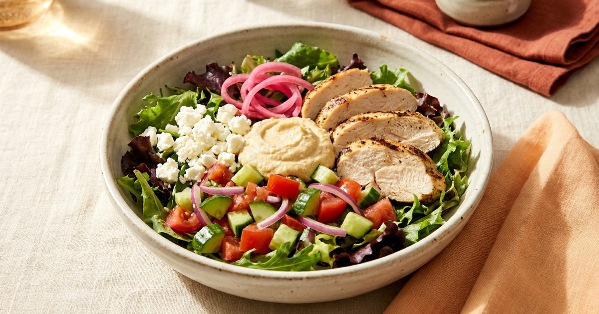A Mediterranean bowl with chicken, hummus, feta, and cucumber tomato salad