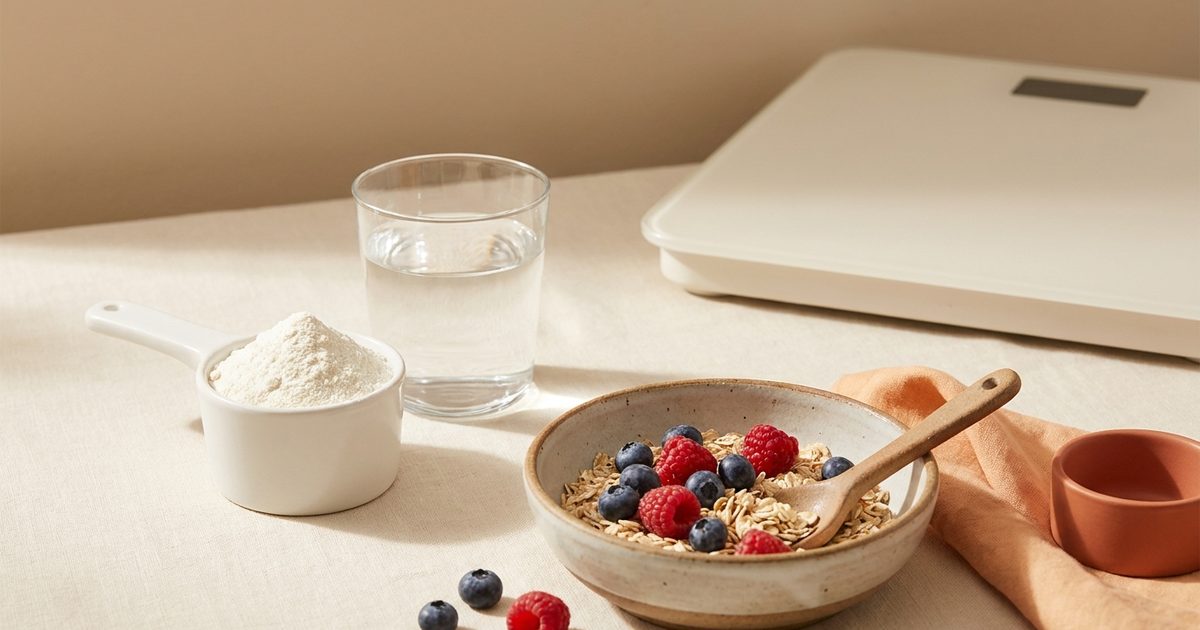 A scoop of white powder next to a glass of water, a breakfast bowl, and the edge of a bathroom scale